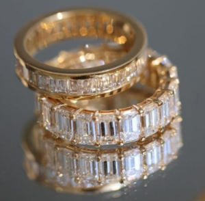 Two diamond eternity bands with different carats are stacked on a mirror.
