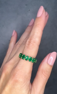 A woman is showing a green emerald eternity ring.